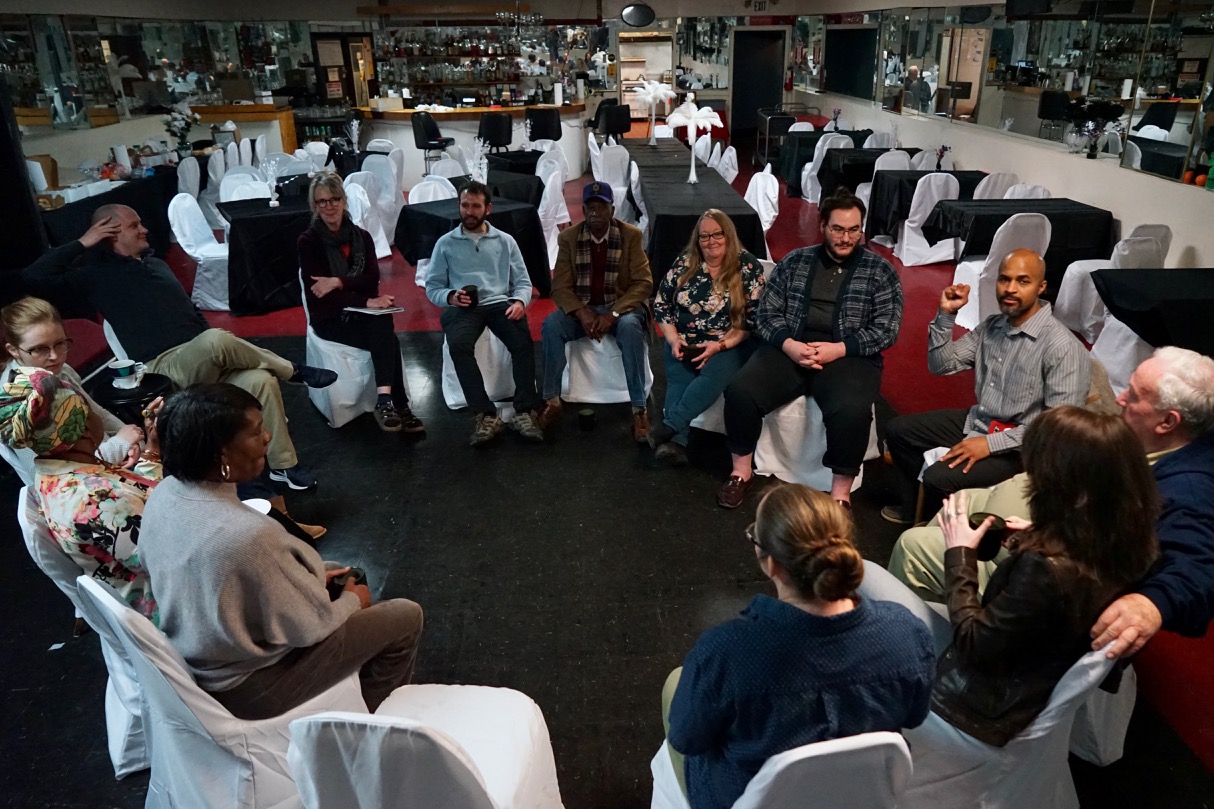 A group of people sitting in white chairs arranged in a circle.