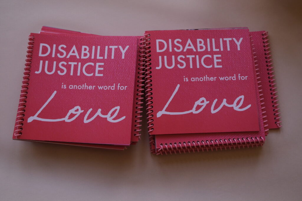 Square red spiral-bound notebooks reading, "Disability justice is another word for love."