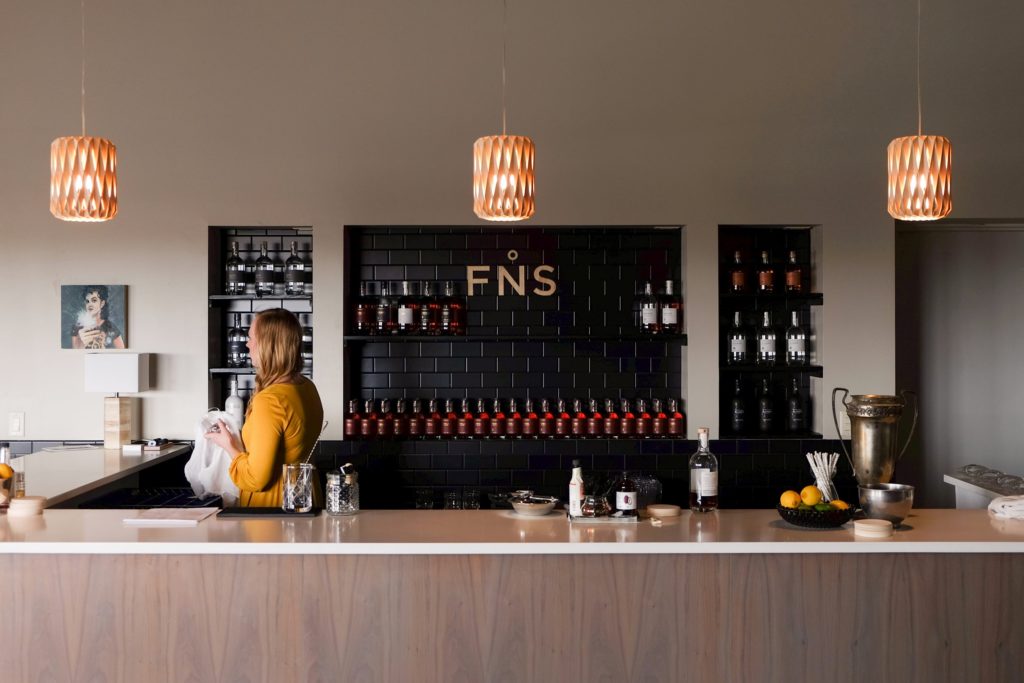 A room with a long bar and a wall behind it with bottles of whiskey on shelves.