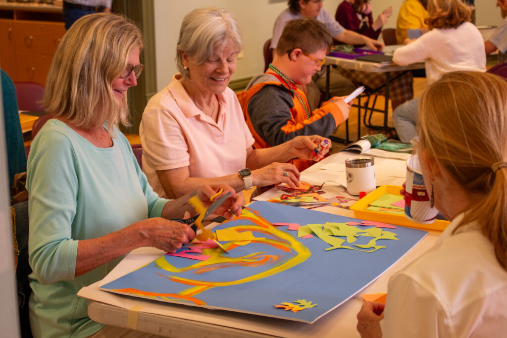 Four people sitting around a table painting and cutting up colored paper.