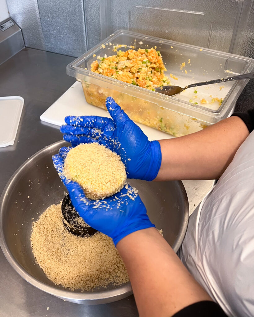 A person wearing bright blue latex gloves in the process of making a round patty.