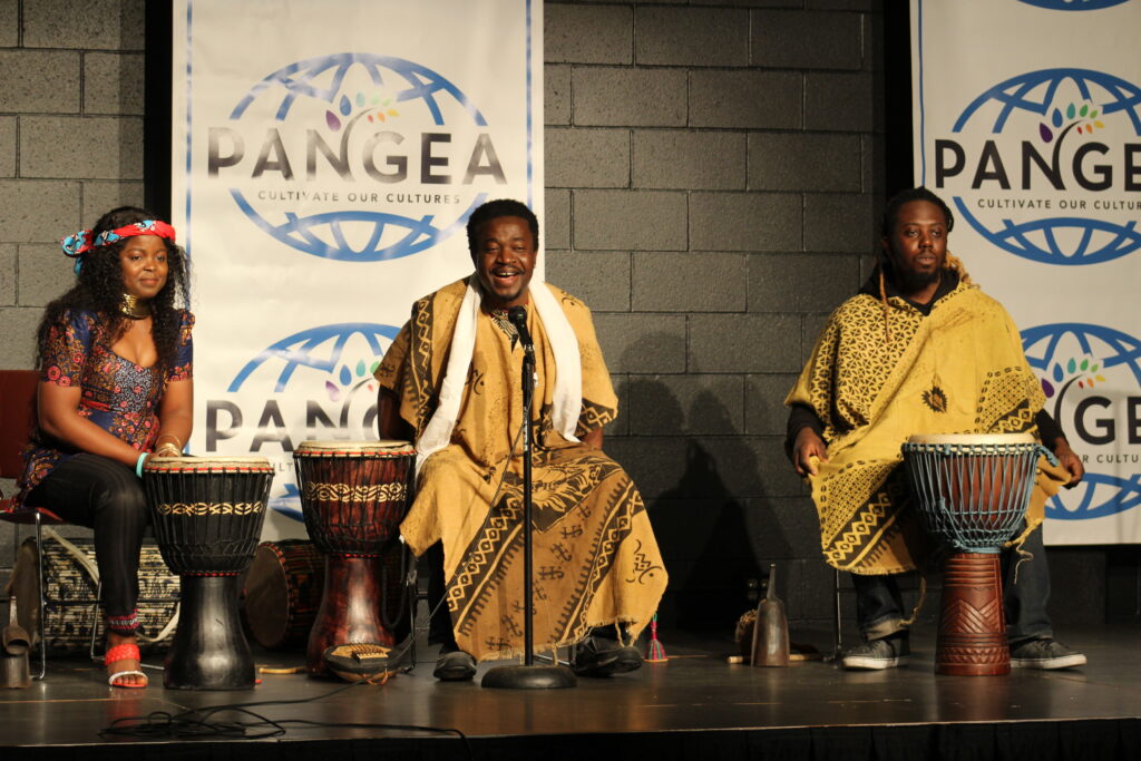 Three people of dark skin tone on stage with African drums.