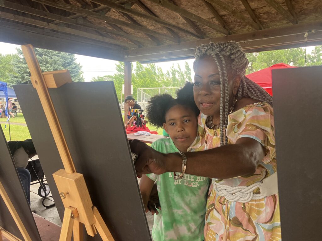 Two people of dark skin tone, one young and one old, look at a sign on an easel