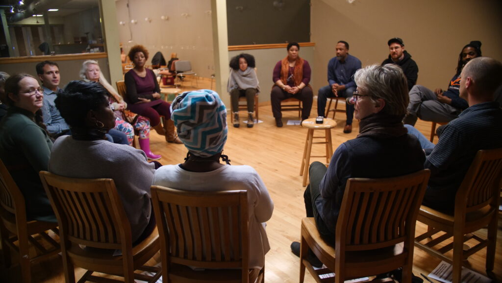 A group of people sitting in wooden chairs arranged in a circle.