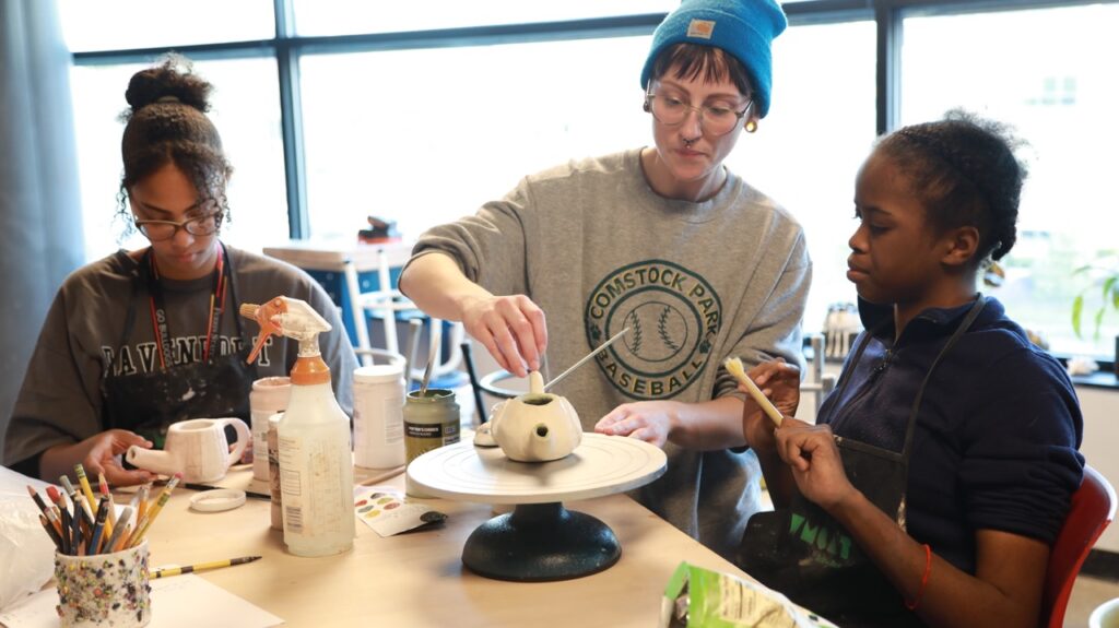 Three people work in a ceramics studio making teapots.