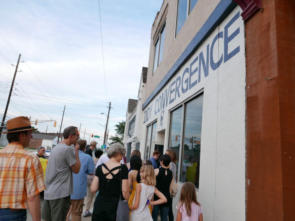 A group of people filter into a building with Indy Convergence written on the side