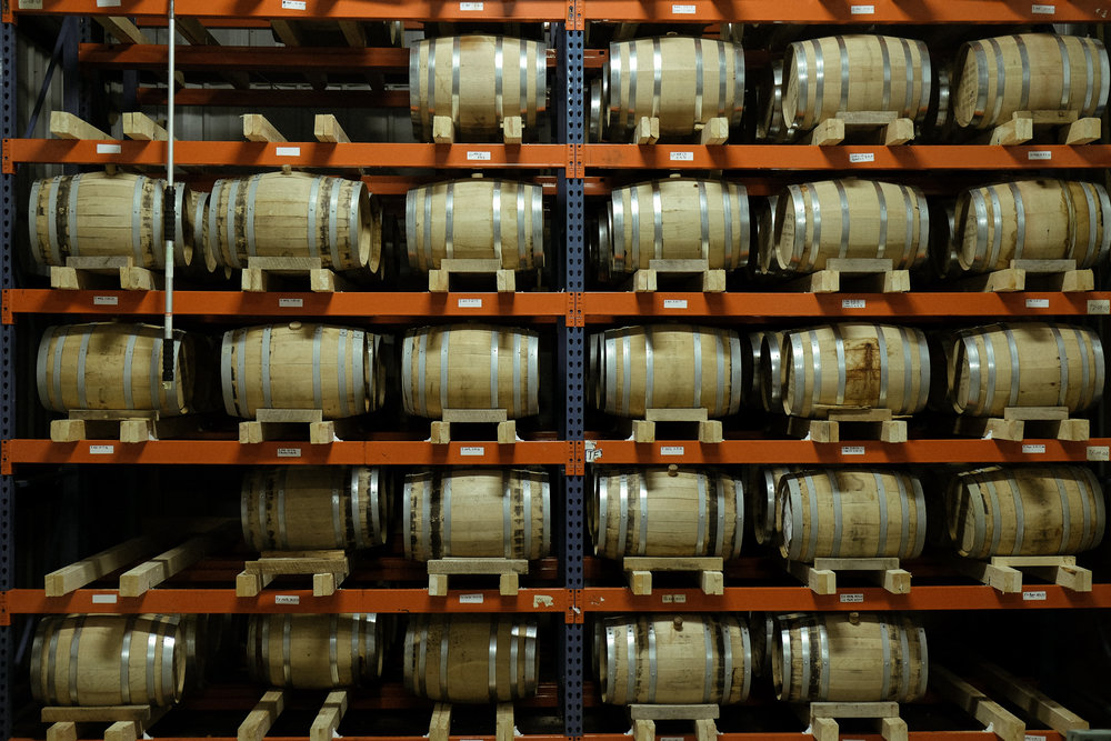 Wooden barrels stacked on a tall multi-level, industrial metal shelf.