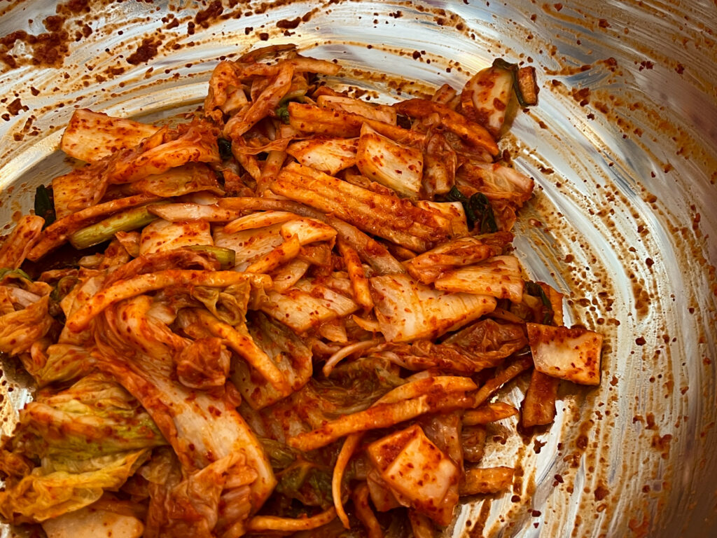 A pile of bright red napa cabbage kimchi inside of a metal bowl.