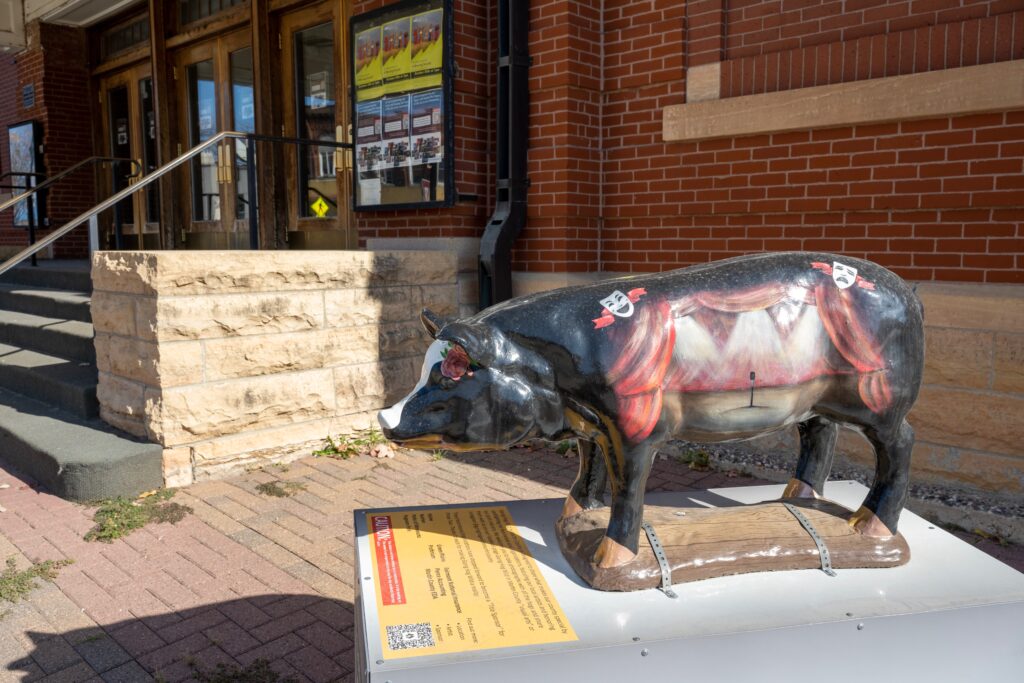 A pig statute with a stage painted on it sits outside of a brick building