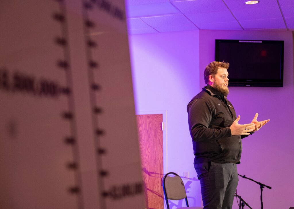 A white man speaks to an audience with his hands held out