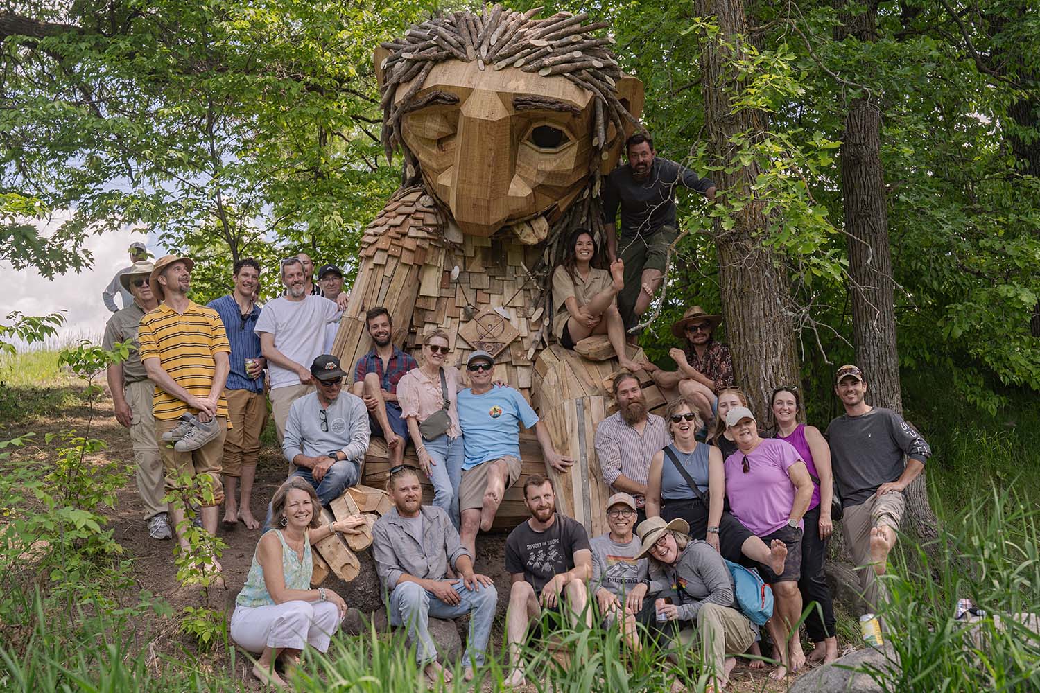 A group of people stand by a giant wooden troll statue in the woods