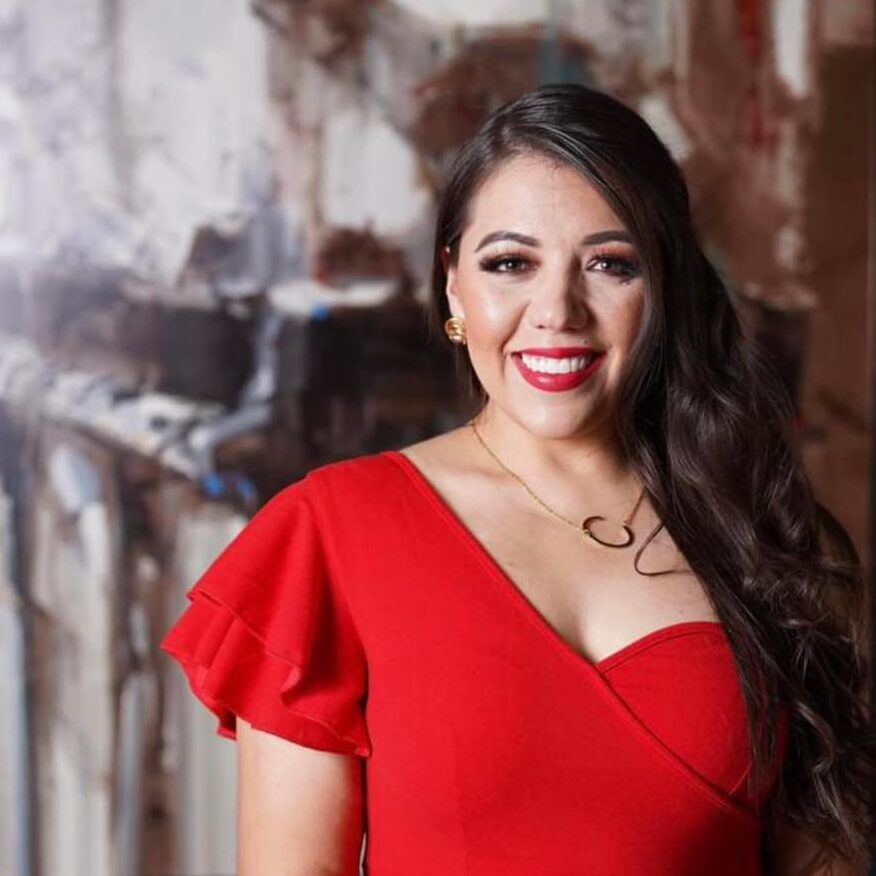 A person of medium skin tone with long hair smiling. They are wearing a red top.