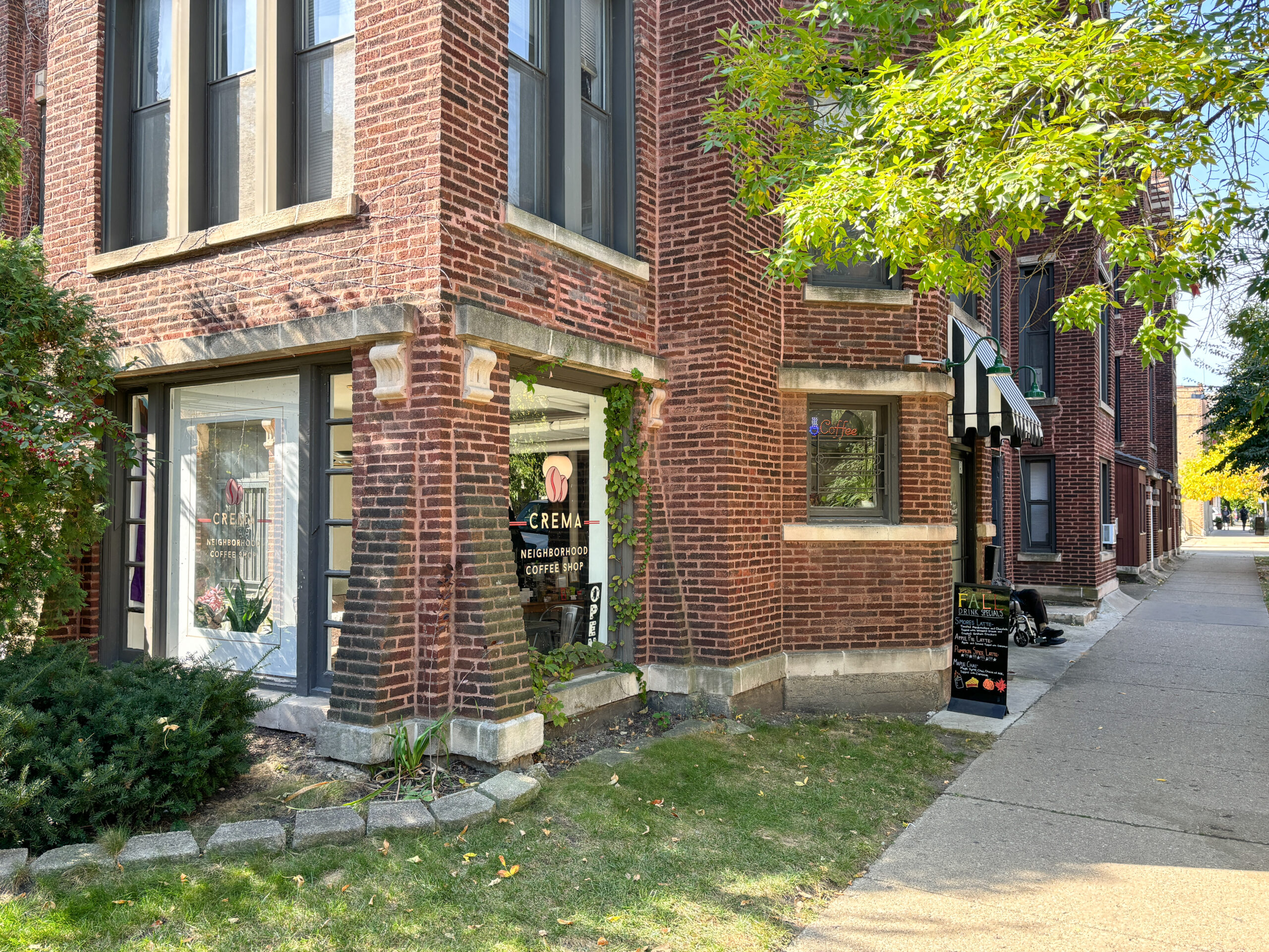 A brick building with the ground floor with large windows. There is signage on the windows that read "Crema, Neighborhood Coffee Shop"