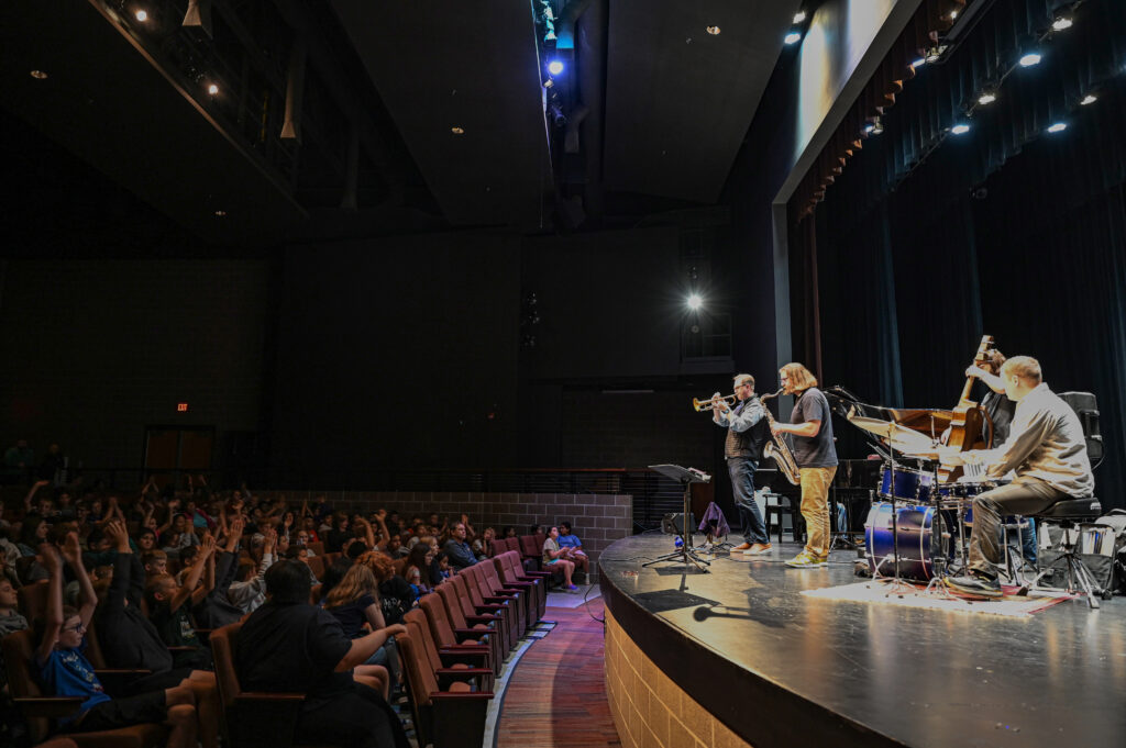 A jazz group plays for an excited student audience in a school auditorium