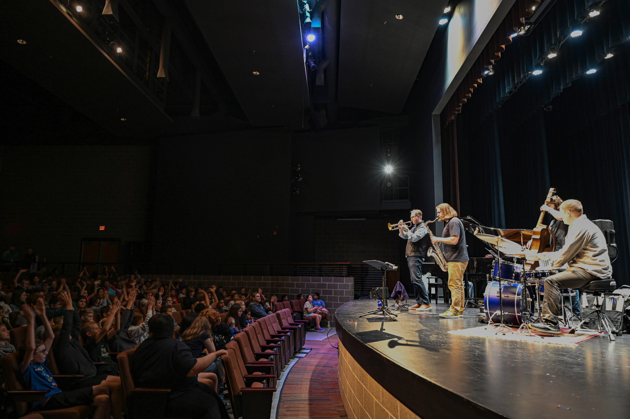 A jazz group plays for an excited student audience in a school auditorium