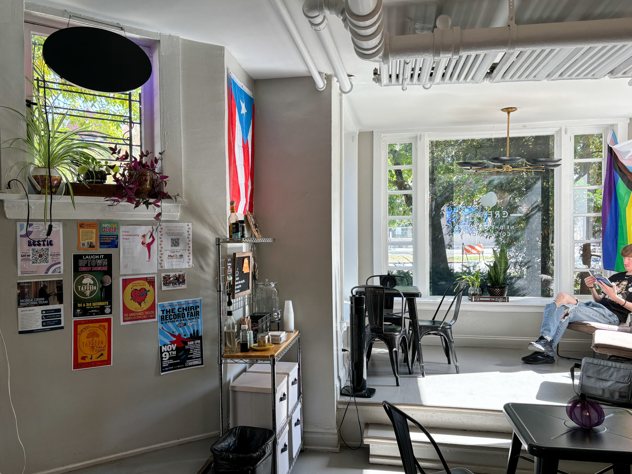 A view of a room with large windows and sets of tables and chairs. One of the walls has posters pasted on it.