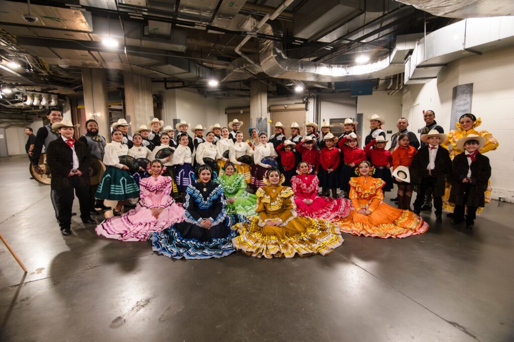 A group of dancers smiling and posing for a photo. Some are dressed in colorful traditional attire.