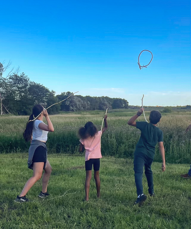 Three young adults holding sticks as they aim for a wooden hoop in the air.