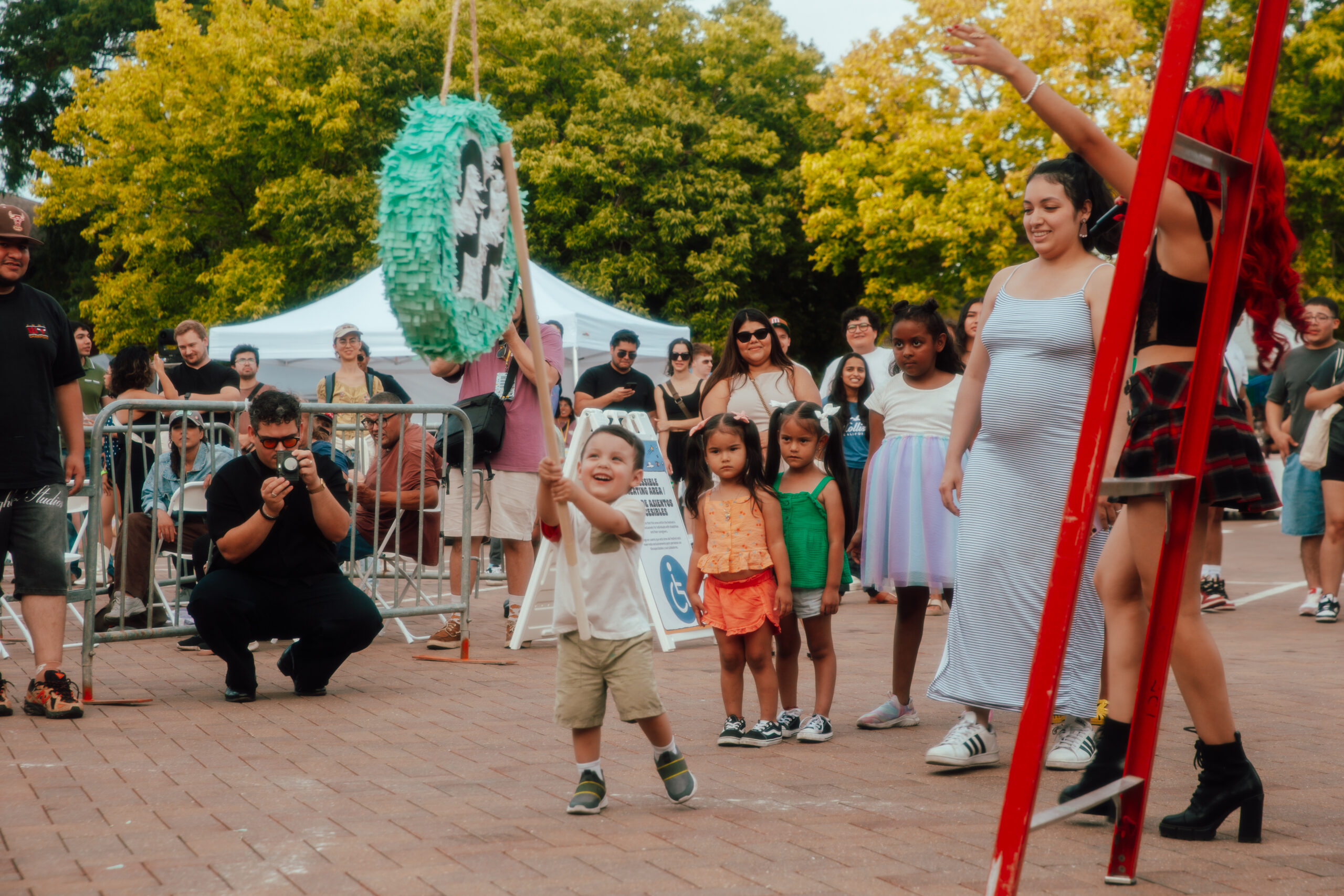 A small child holding a stick as they aim to hit a pinata. Other children and adults look on.