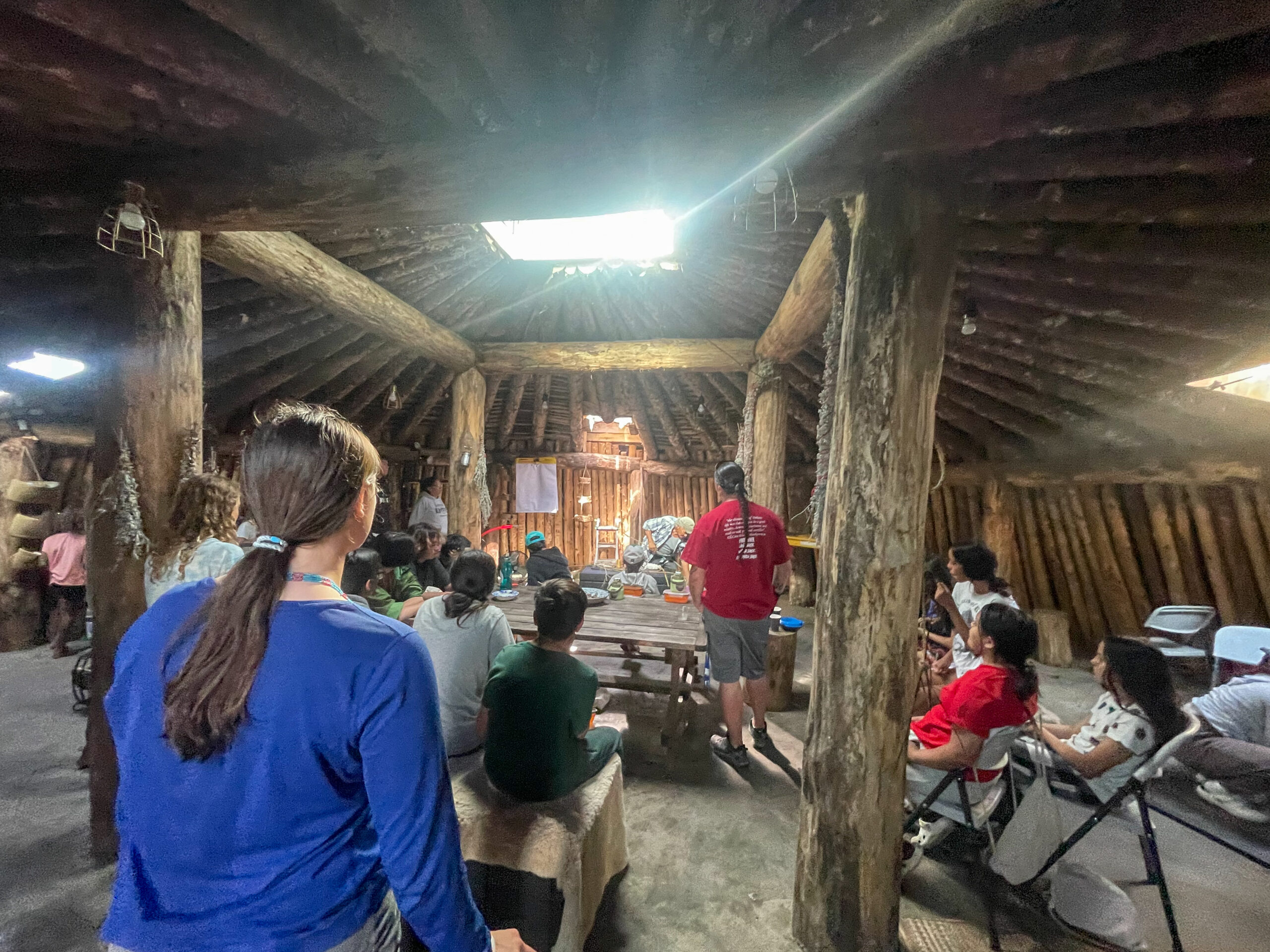 People sitting inside a wooden structure as they look to the front of the room.