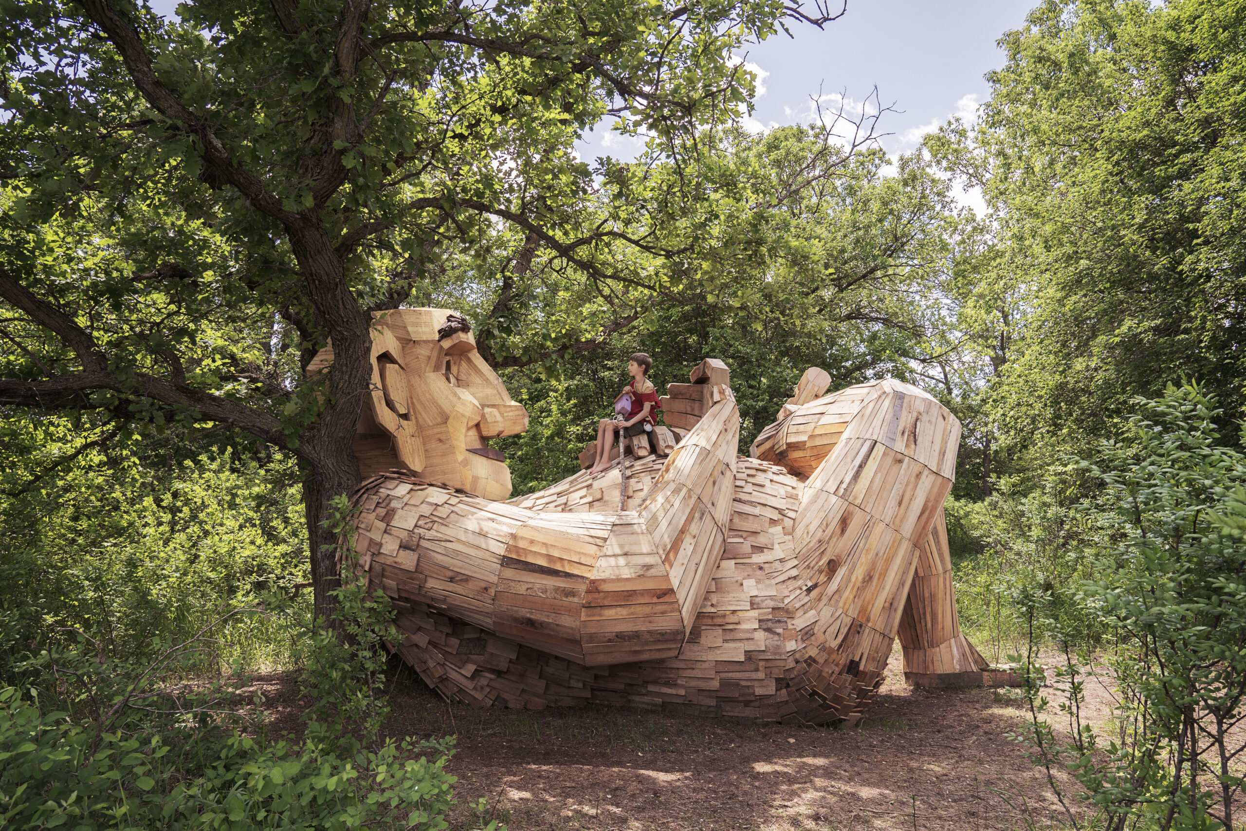 A giant wooden troll leans against a tree