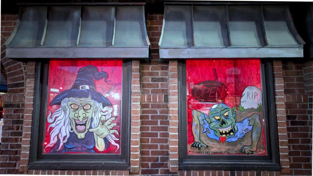 An exterior of a building showing two windows decorated with Halloween-themed art.