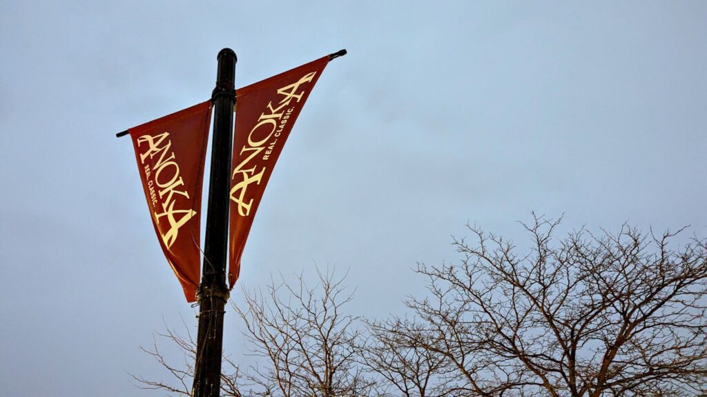 Red triangular signs on a post reading "Anoka" against the sky.