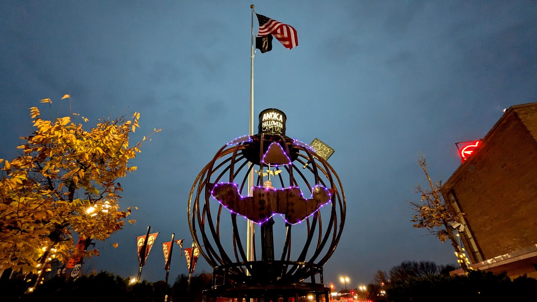 A large jack-o-lantern structure near a flagpole, building, and tree.