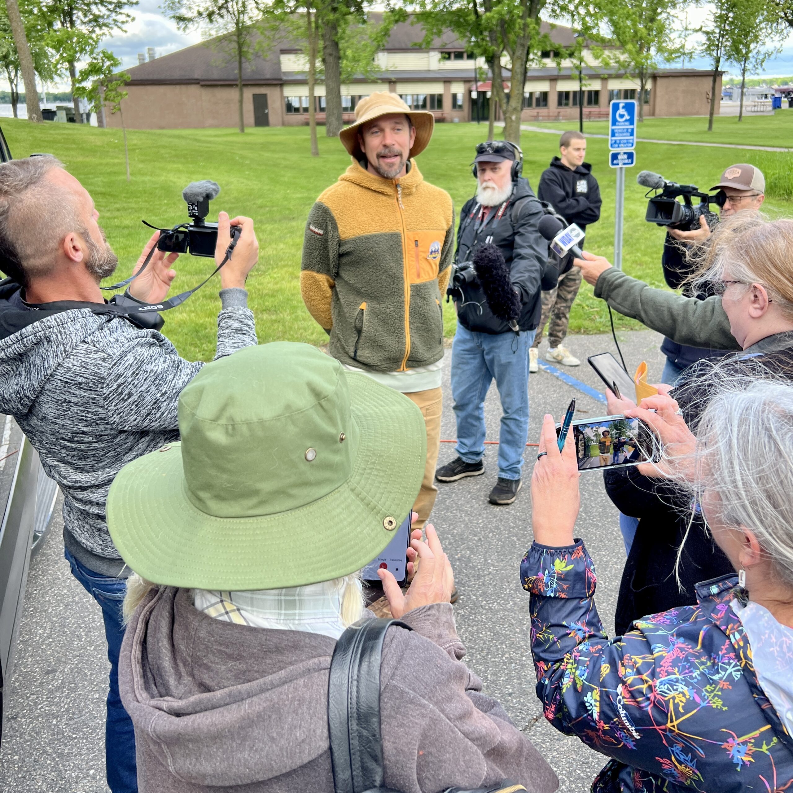 A man in a yellow fleece answers questions from journalists outside