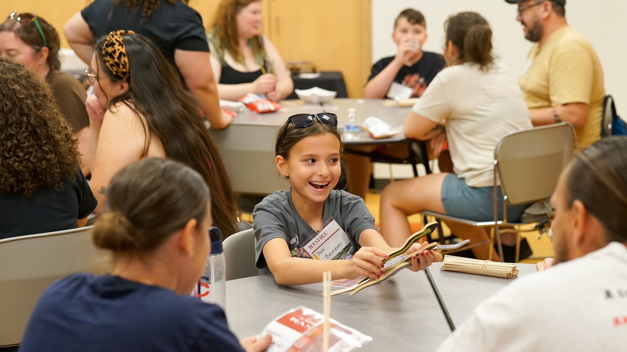 A young person smiles amid people playing a game at a table.