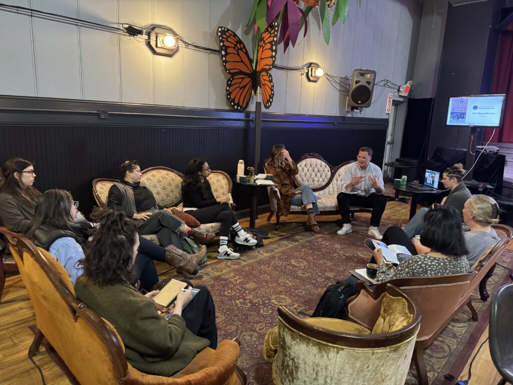 A group of people sitting on vintage sofas and chairs in a circle inside of a large room.