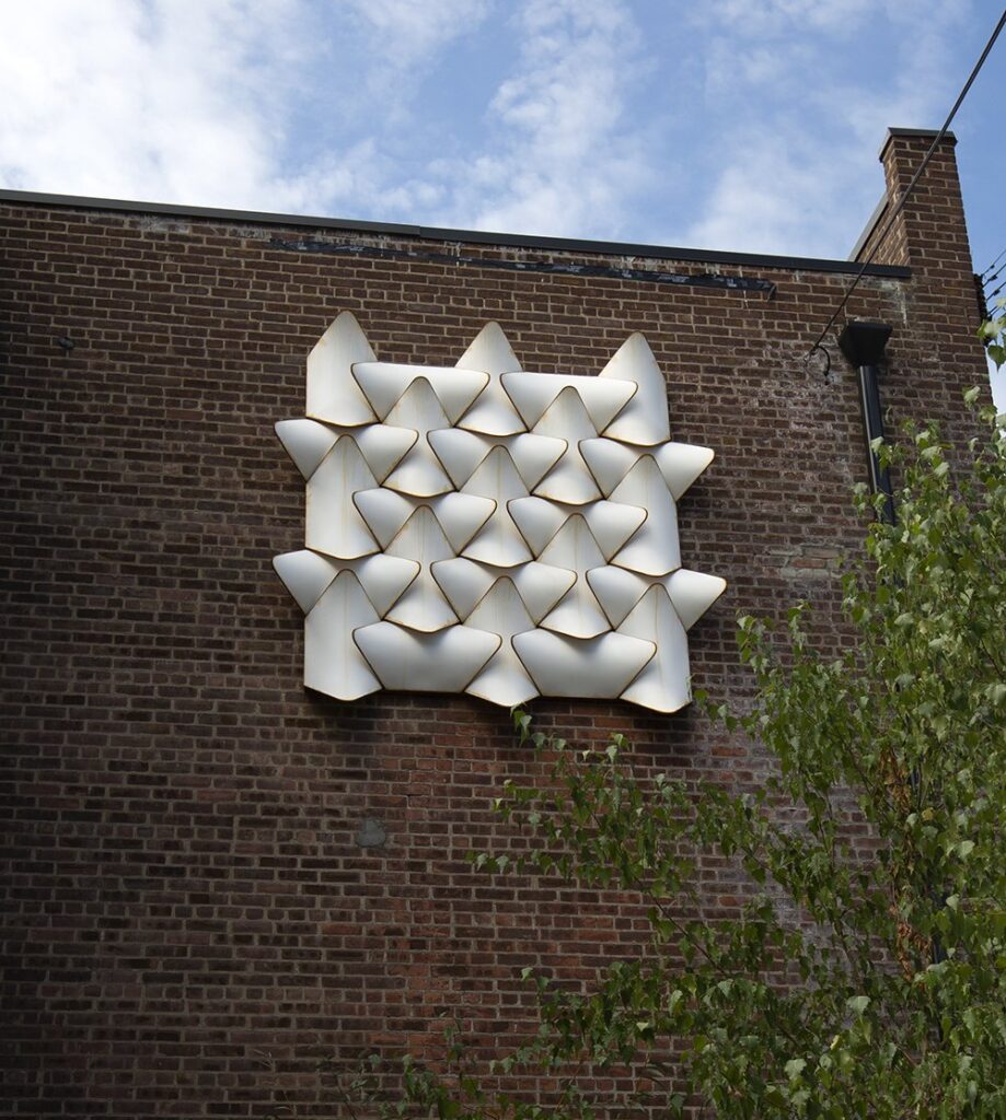 A white geometric three-dimensional sculpture placed on the side of brick building.