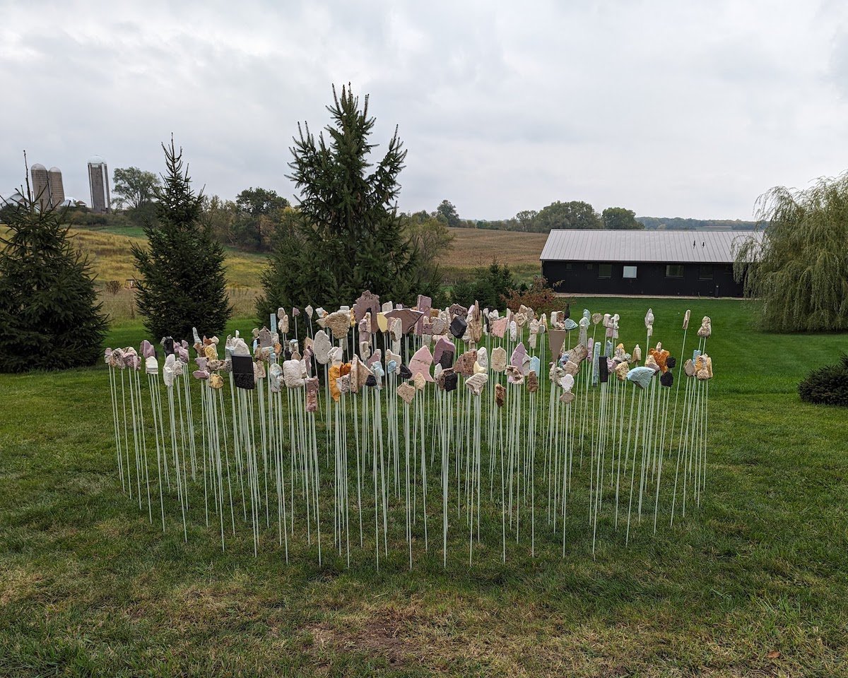 Rock-like objects mounted on top of white sticks are placed together in an outdoor field.