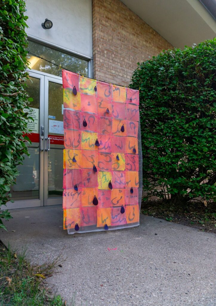 An artwork with red and orange blocks hanging in front of a door of a building.