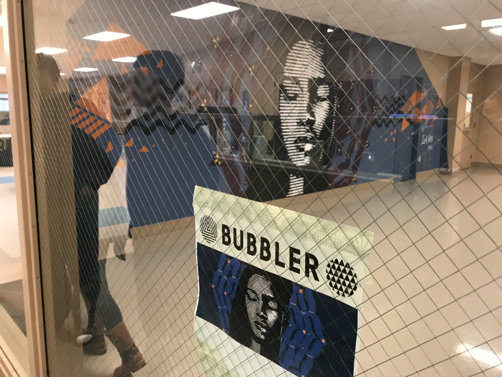 A view through a glass window of a large wall with a mural painting depicting a person's head in black and white colors.