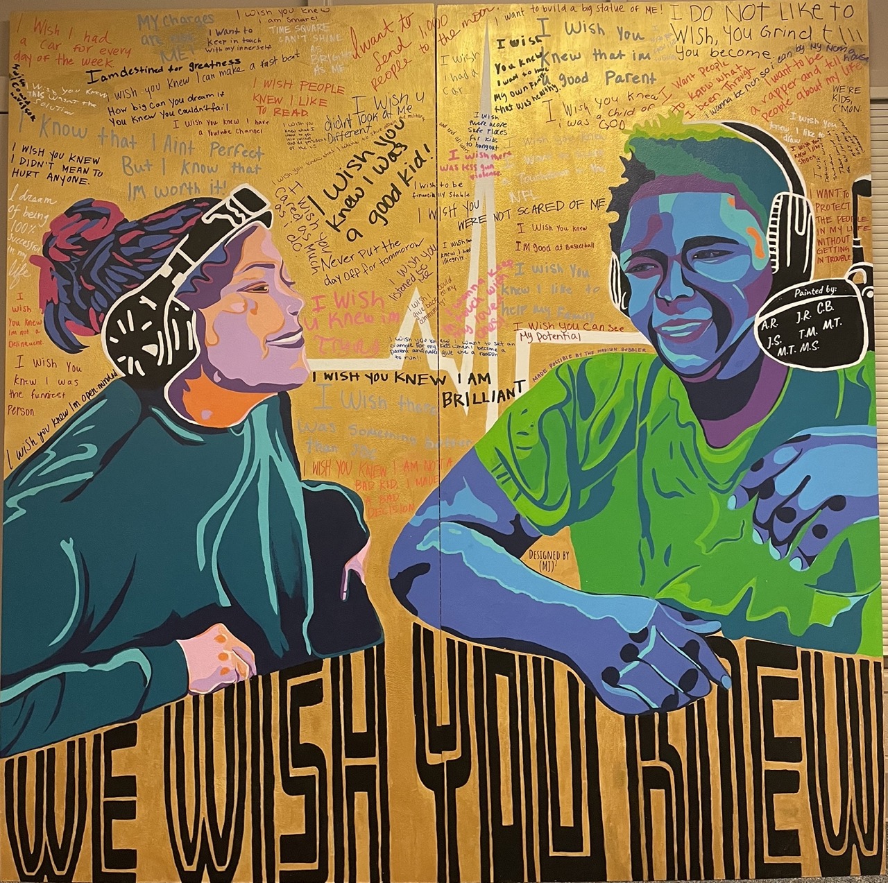 A large wall mural painting depicting two people wearing headphones and with writing all around them. The are large letters that read, 'we wish you knew.'