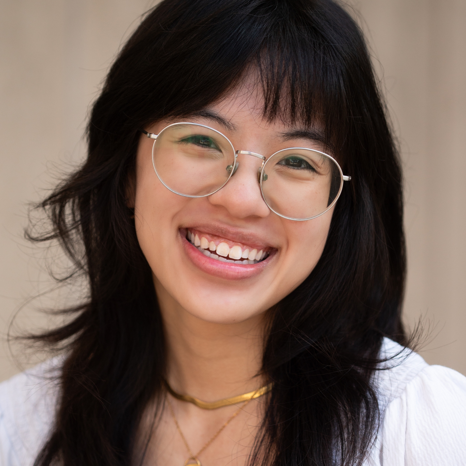 A person of medium light skin tone with long black hair and wire-rimmed glasses, wearing a white top.