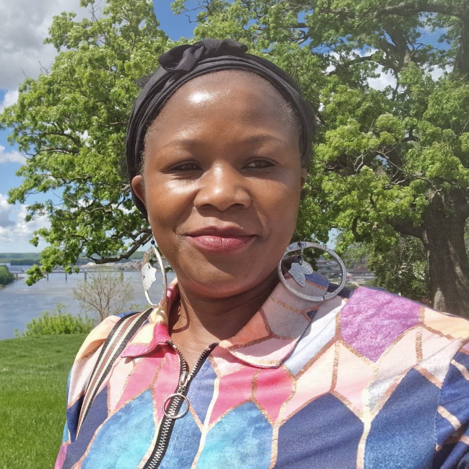 A person of dark skin tone wearing a headscarf, large circular earrings, and a blue and purple color-blocked top