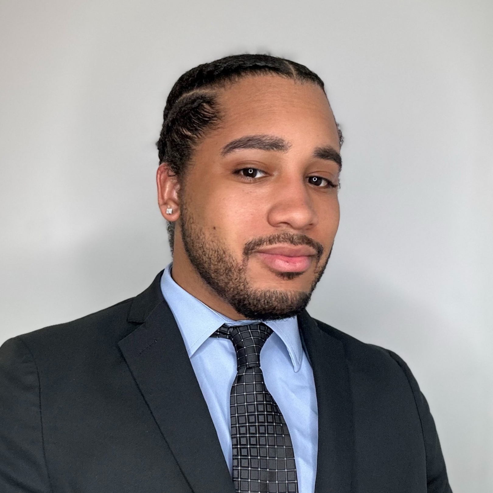 A headshot of a person of medium dark skin tone with black hair, wearing a suit and tie.