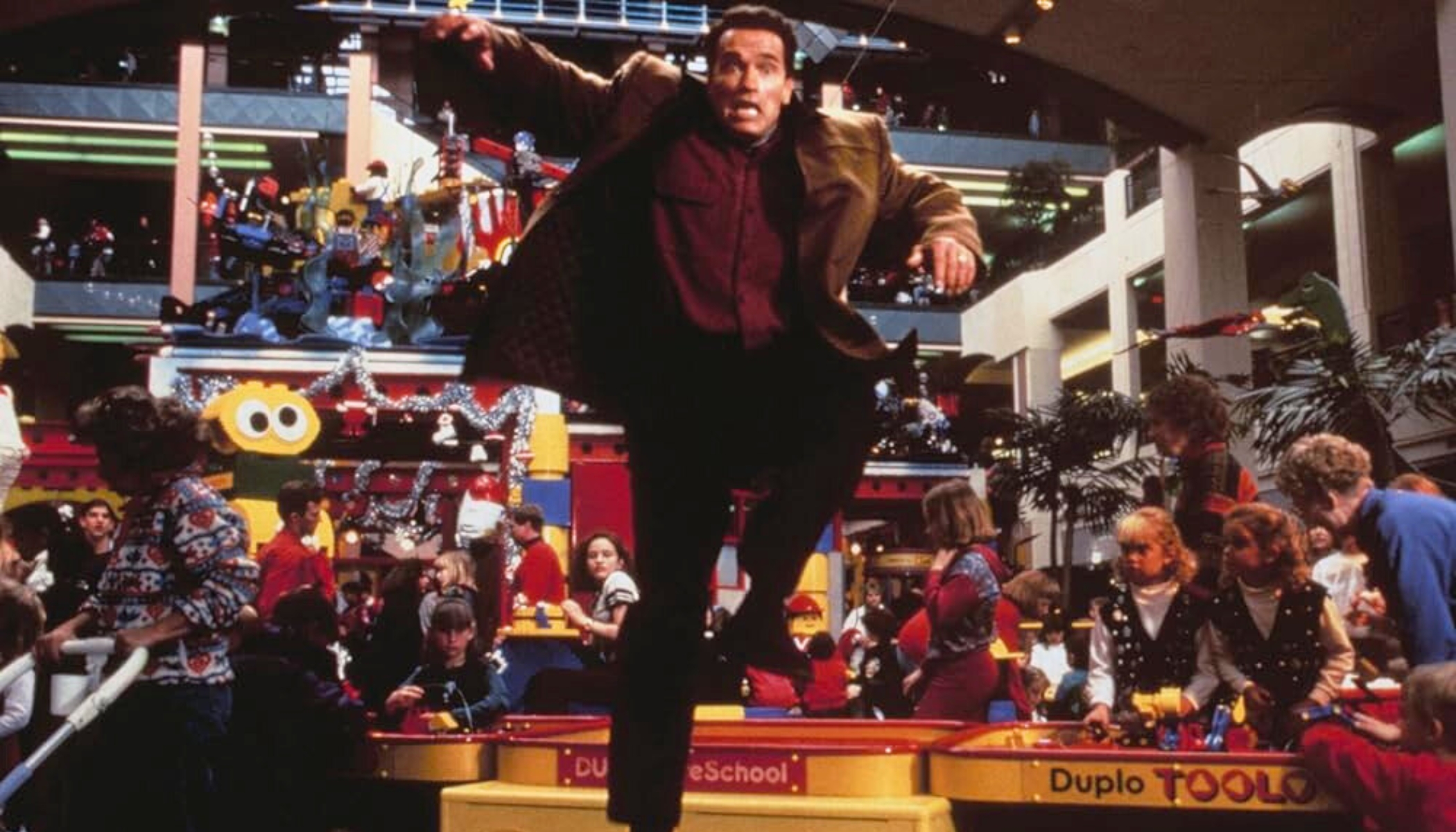 A screengrab from the film Jingle All The Way of a person inside a shopping mall, jumping over a Duplo blocks set.