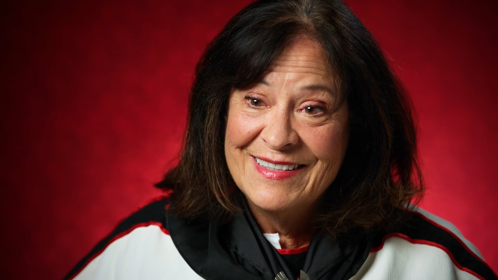 Medium-skin-toned woman with dark hair smiles in front of a red background.