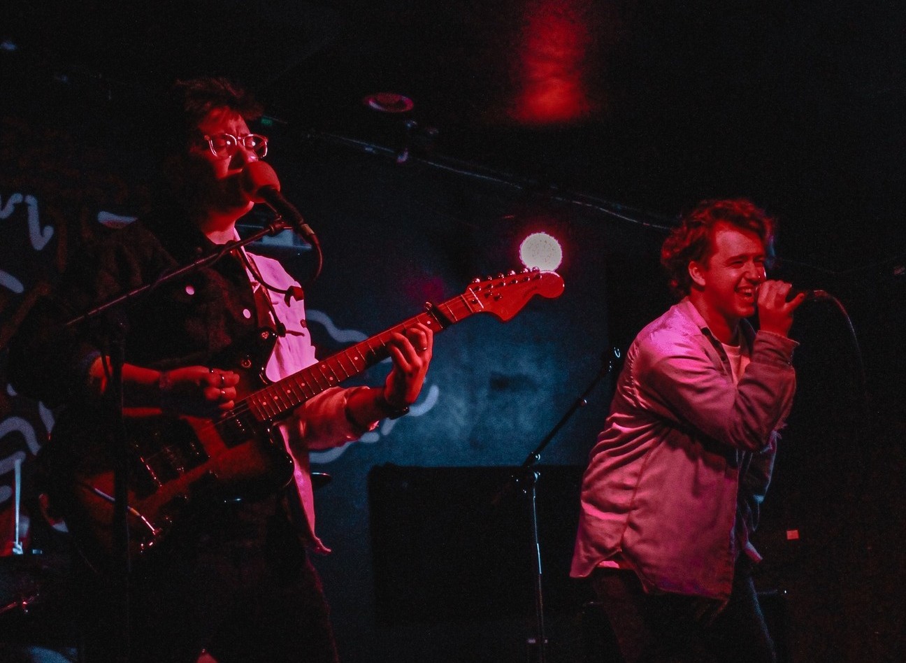 Two musicians perform and sing on a dark stage.