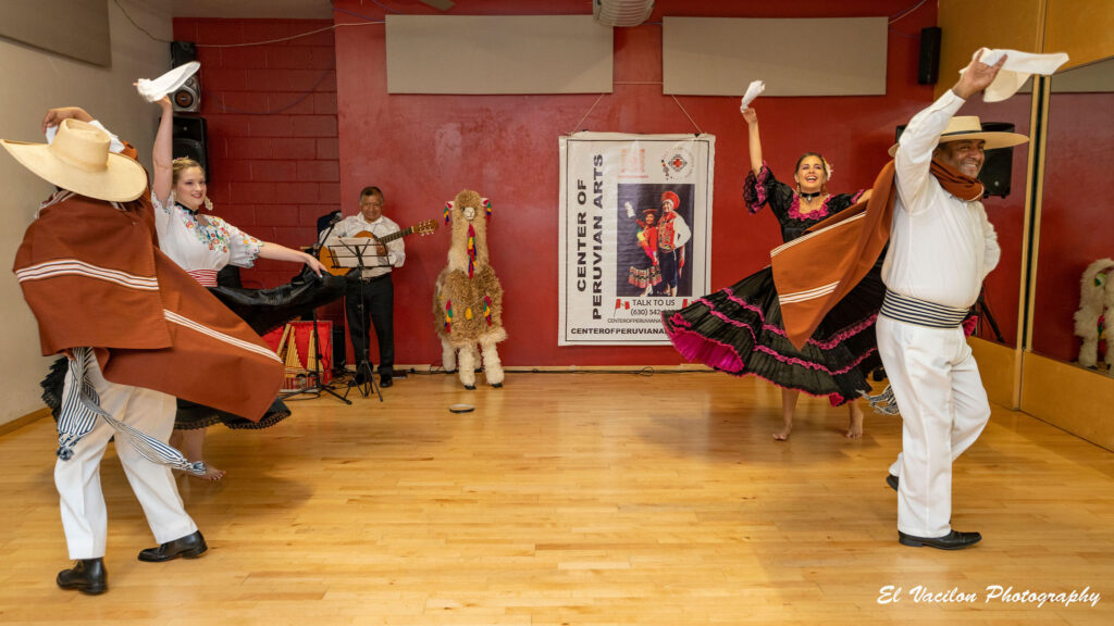 Two male and two female students dressed in traditional Peruvian outfits dance with arms raised in a studio.