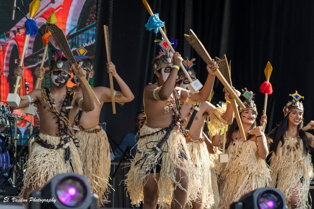 A group of dancers in Peruvian dance costumes carrying torches, pots of water, and spears.