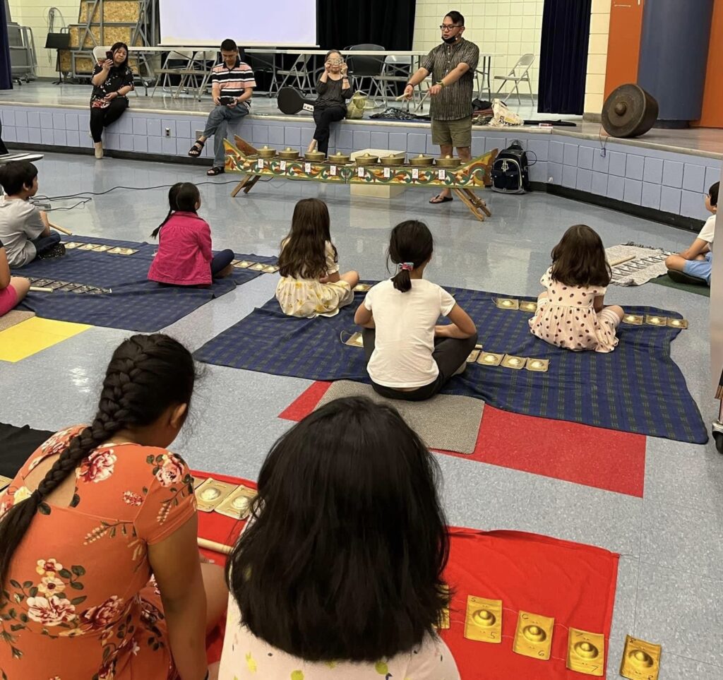 An instructor at the front of the room demonstrating kulintang for a room of seated children.