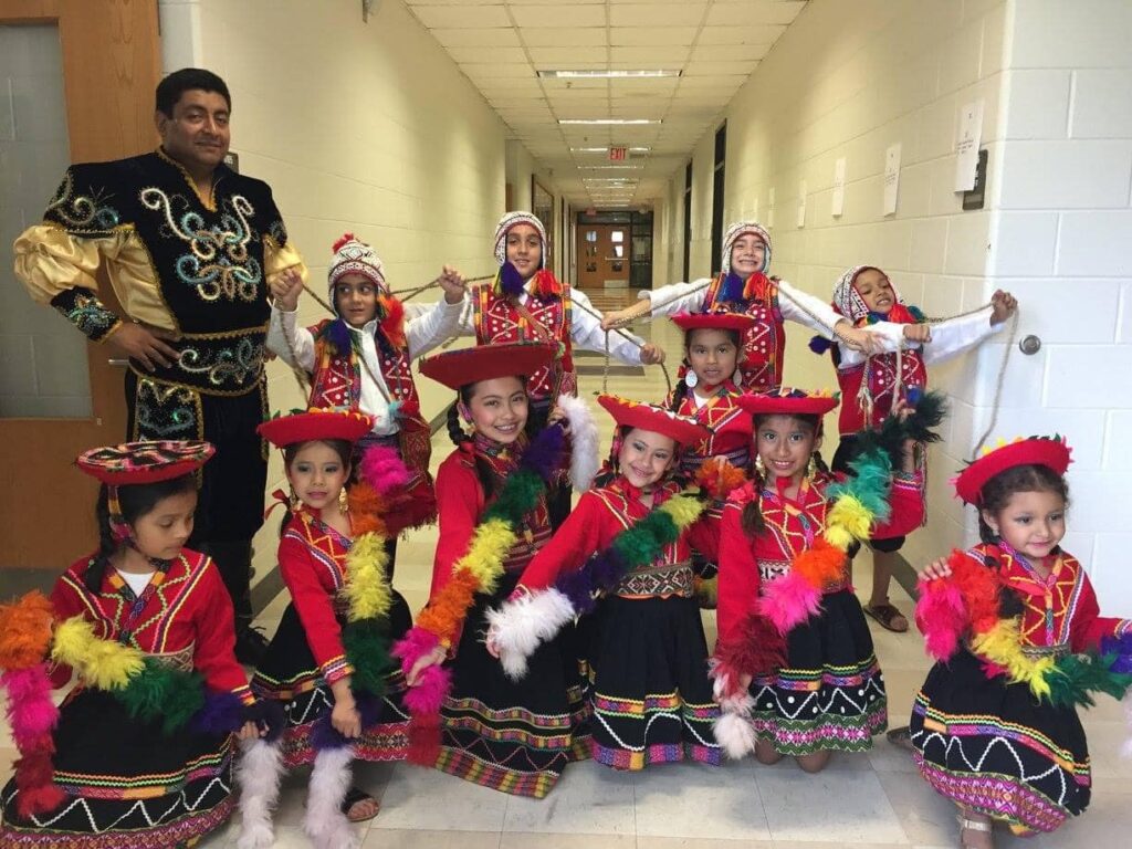 A group of young dancers dressed in colorful traditional Peruvian outfits posing with an adult instructor.