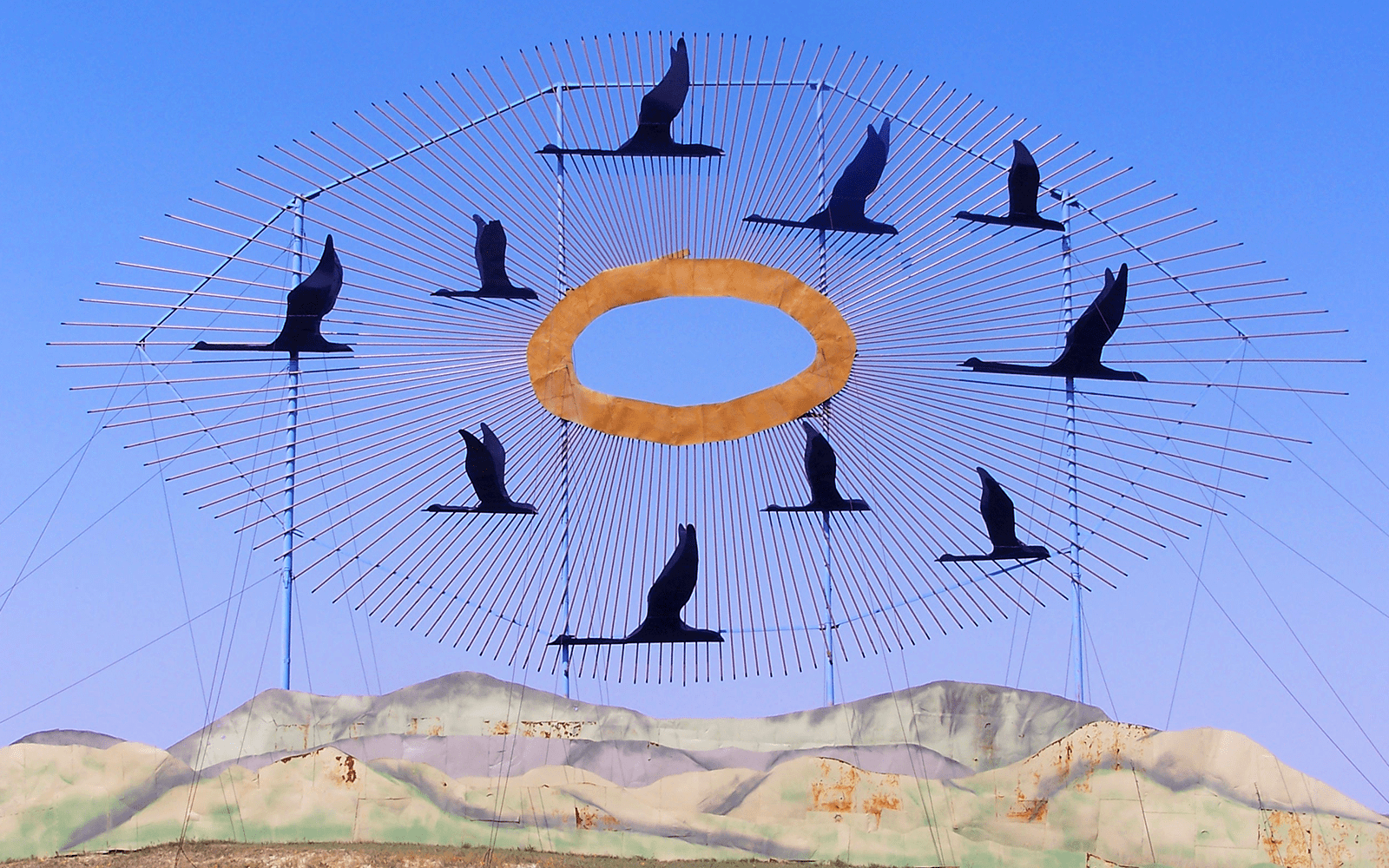 A sculpture of birds, an orange circle and hills against a blue skuy.