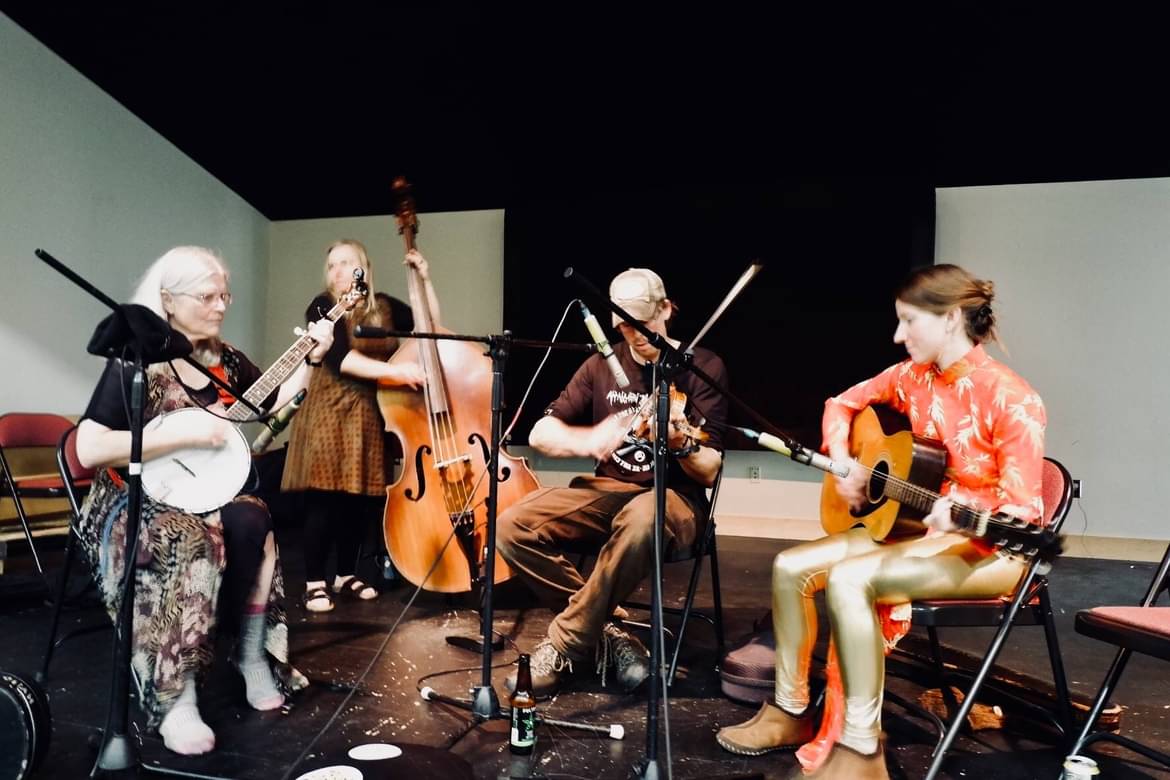 Four musicians play and sit on a stage.