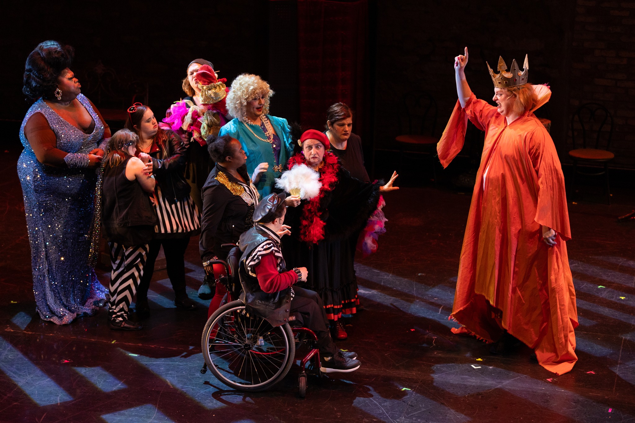 Actors wearing costumes gather on stage in dark lighting.