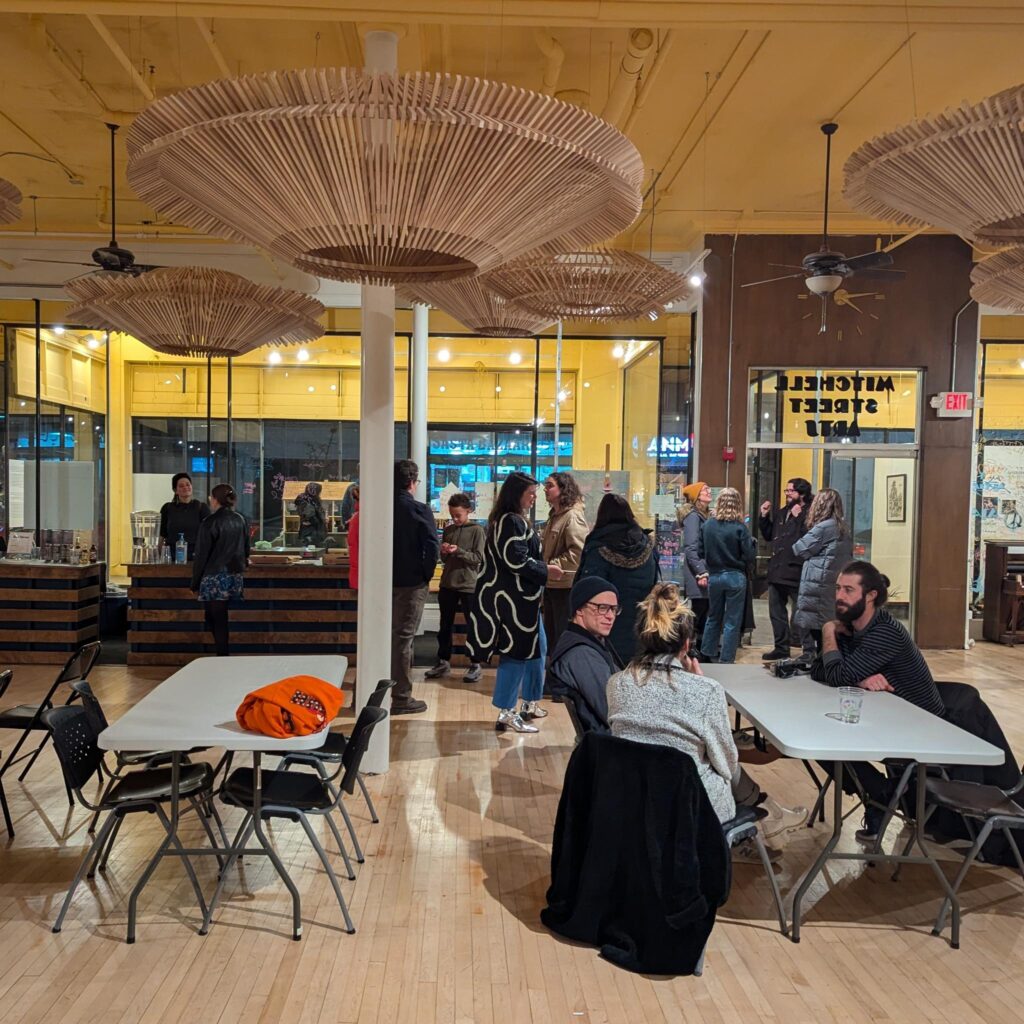 A group of people standing and talking and sitting at folding tables in a lobby space.